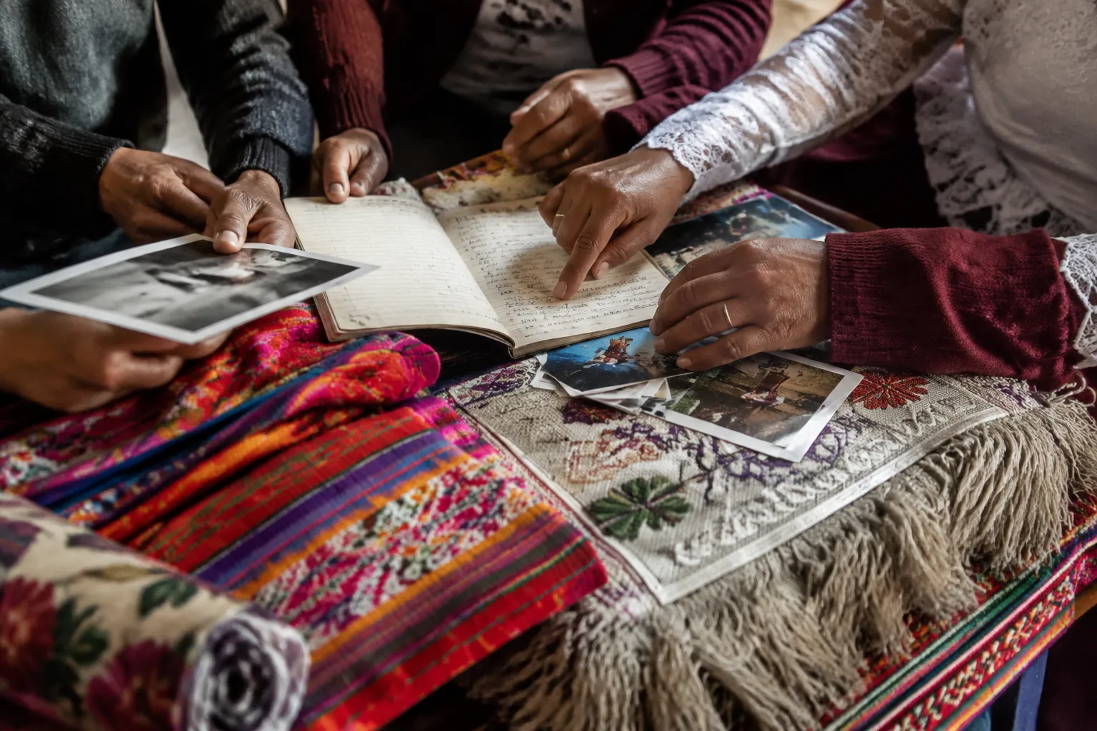Family hands reviewing wedding ceremony notes beside meaningful textiles and printed photographs